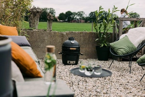 Gratar Kamado Compact Inferno afara in gradina pe pietris langa canapea, masuta si fotolii.