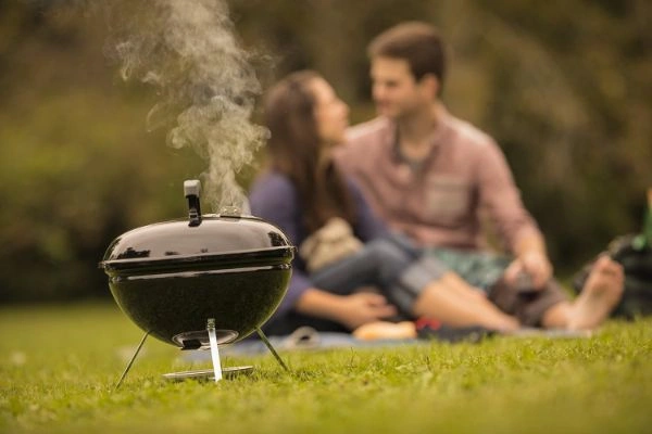 Cuplu in fundal la picnic in natura cu gratar pe carbuni